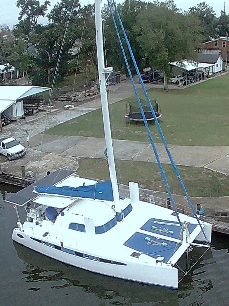 Slide: The Image of 2002 Dolphin 43 catamaran docked by a grassy shore with trees and buildings. - 14
