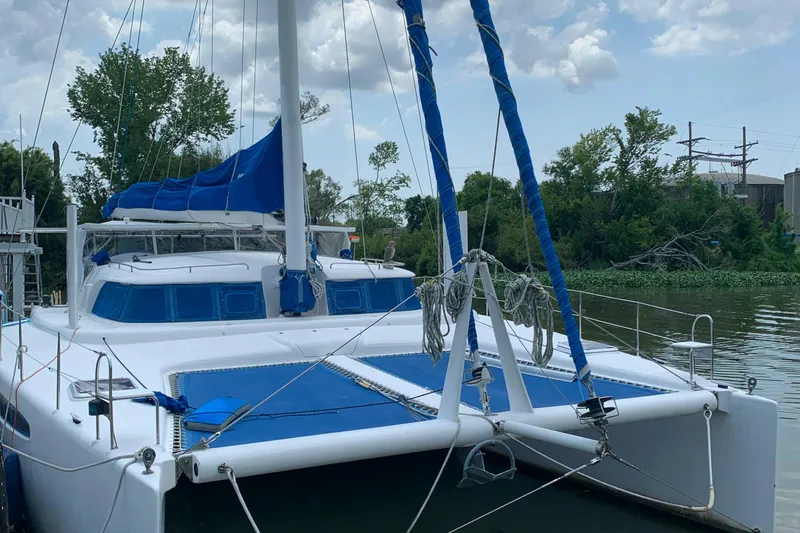 Slide: The Image of 2002 Dolphin 43 catamaran with blue sails docked on a calm river. - 44