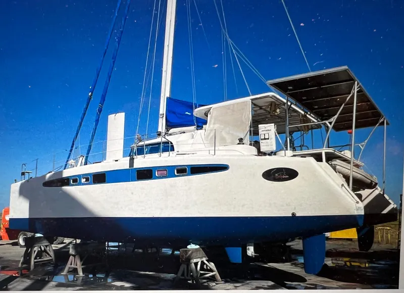 Slide: The Image of 2002 Dolphin 43 catamaran on dry dock, blue and white hull, clear sky background. - 5
