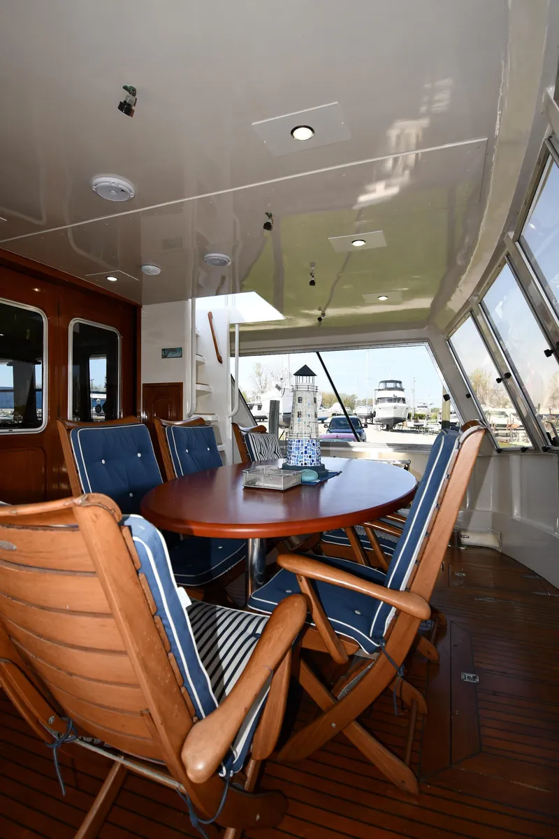 Slide: The Image of 1986 Lowland 64 Pilot House Long Range Motor Yacht interior dining area with wooden table and cushioned chairs. - 18