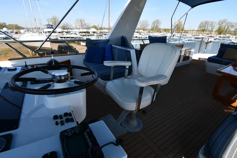 Slide: The Image of 1986 Lowland 64 Pilot House Long Range Motor Yacht helm station with white captain's chair and marina view. - 33