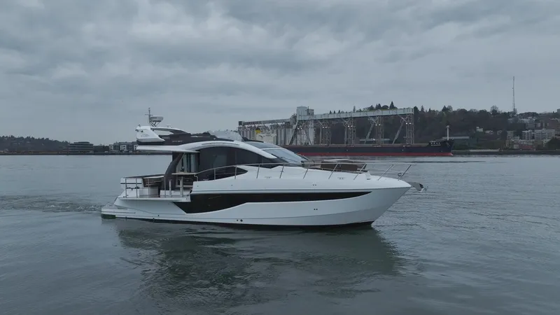 Slide: The Image of 2024 Galeon 470 Sky yacht cruising on a cloudy day near industrial waterfront. - 5