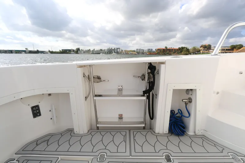 Slide: The Image of 2012 Intrepid 475 Sport Yacht deck with storage compartments and water hose, overlooking calm waters. - 16