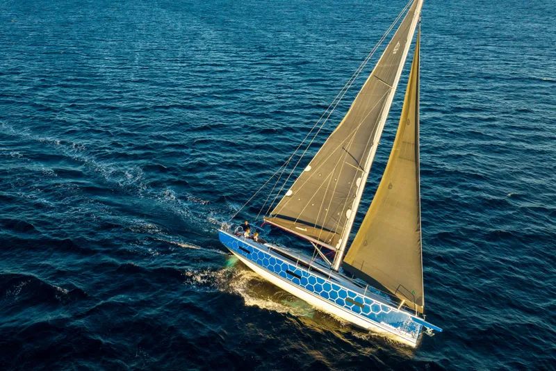 Slide: The Image of 2026 Dehler 46 yacht sailing near rocky coastline with lush greenery. - 57