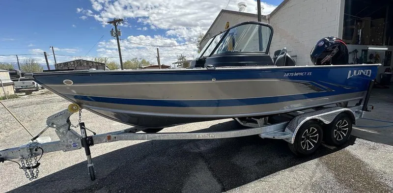 Slide: The Image of 2024 Lund 1875 Impact XS Sport boat on a trailer under a partly cloudy sky. - 3