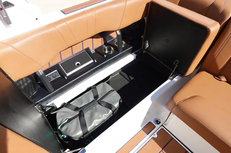 Slide: The Image of 2023 Malibu Wakesetter 24 MXZ boat interior storage compartment with brown seats and a duffel bag. - 26