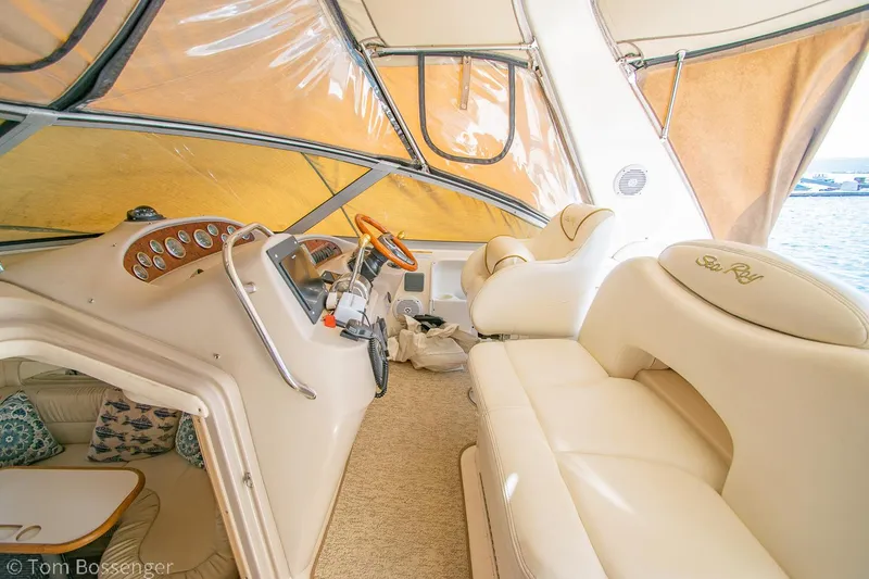 Slide: The Image of 1999 Sea Ray 340 Sundancer interior with beige seating and helm, featuring a sunny view. - 23