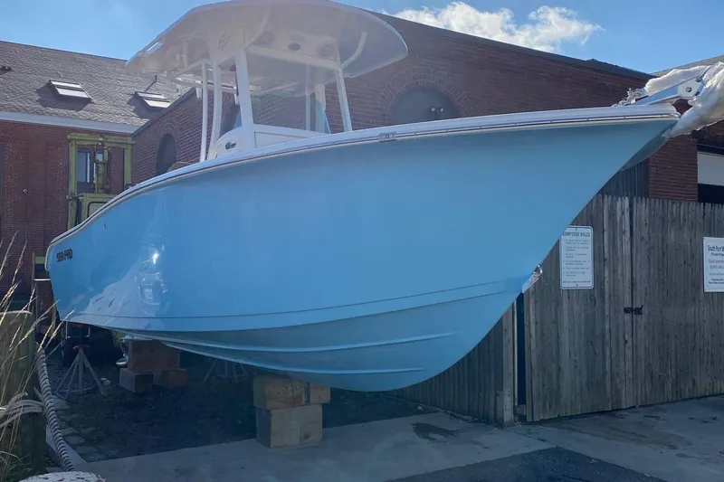 The Image of 2024 Sea Pro 242 boat in light blue, docked near a wooden fence and brick building. - 1