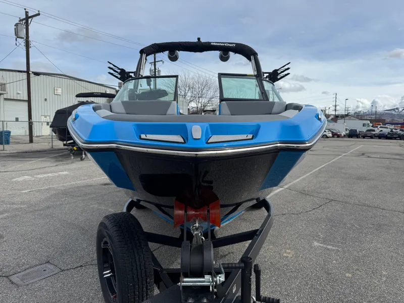 Slide: The Image of 2024 MasterCraft NXT23 boat in a parking lot, front view, blue and black design. - 2