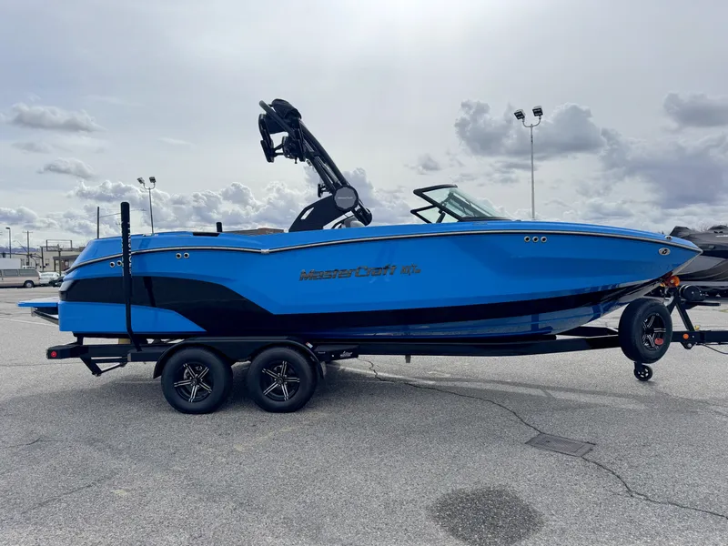 Slide: The Image of 2024 MasterCraft NXT23 boat in vibrant blue on a trailer, parked outdoors. - 3