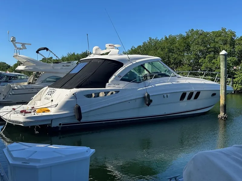 The Image of 2006 Sea Ray 48 Sundancer yacht docked in a marina, surrounded by water and greenery. - 0