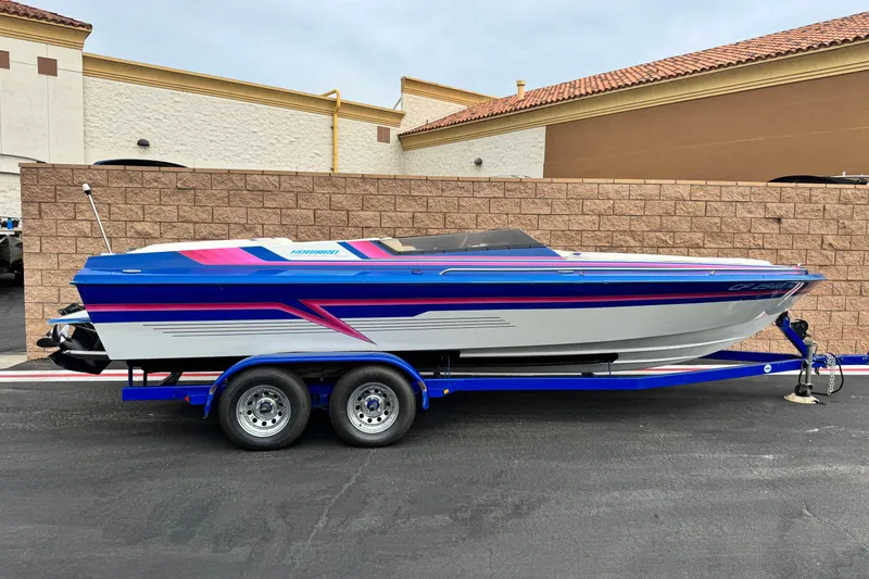 The Image of 1994 Howard 22 Bowrider boat on trailer, featuring vibrant blue and pink accents. - 0