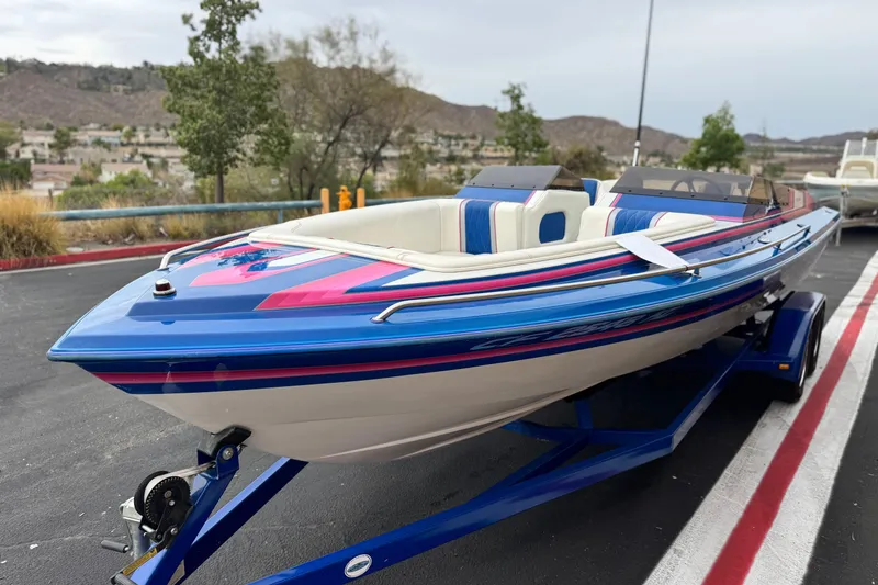 Slide: The Image of 1994 Howard 22 Bowrider boat with vibrant blue and pink design on a trailer. - 3