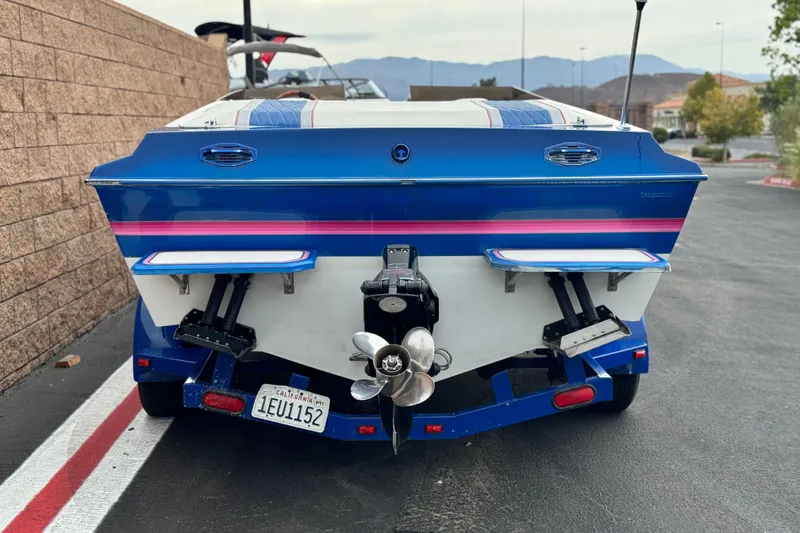 Slide: The Image of 1994 Howard 22 Bowrider boat, blue with pink stripe, parked on asphalt. - 4
