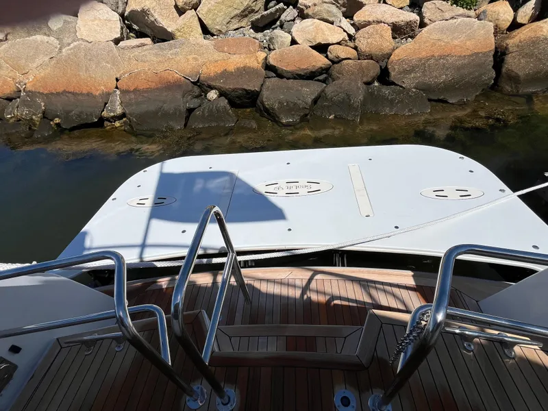 Slide: The Image of 1999 Hatteras 74 Sport Deck Motor Yacht stern view with swim platform and rocky shoreline. - 20