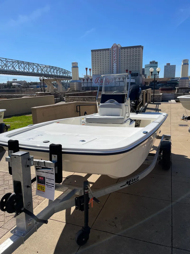 Slide: The Image of 2024 Mako Pro Skiff 13 CC boat on a trailer, displayed outdoors near a bridge and buildings. - 2