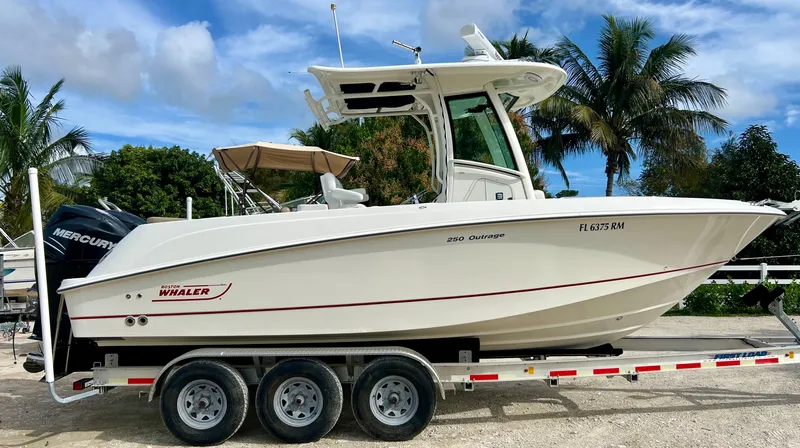Slide: The Image of 2015 Boston Whaler 250 Outrage boat on a trailer with palm trees in the background. - 0