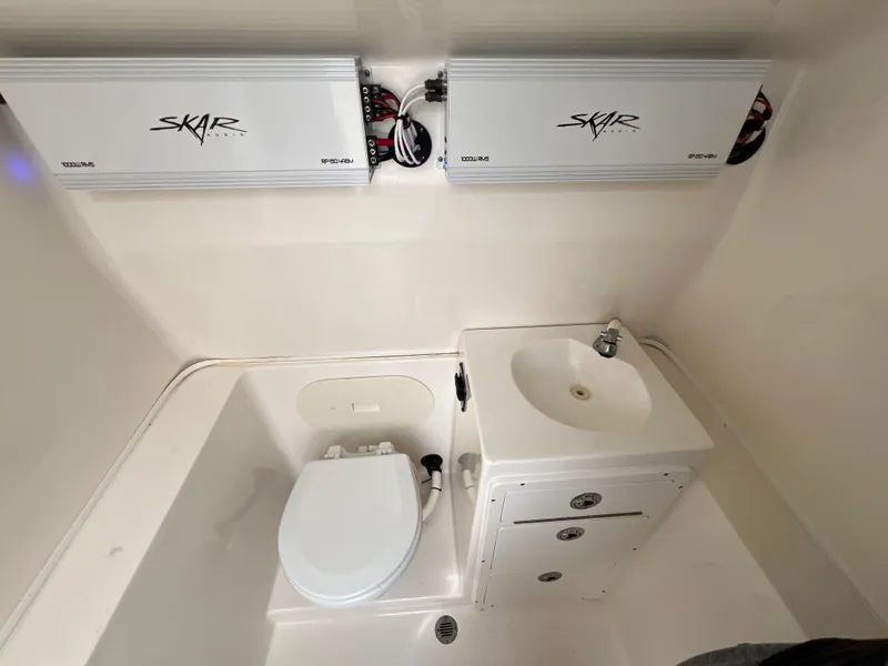 Slide: The Image of 2014 Cobia 296 Center Console boat bathroom with toilet, sink, and Skar audio equipment. - 34