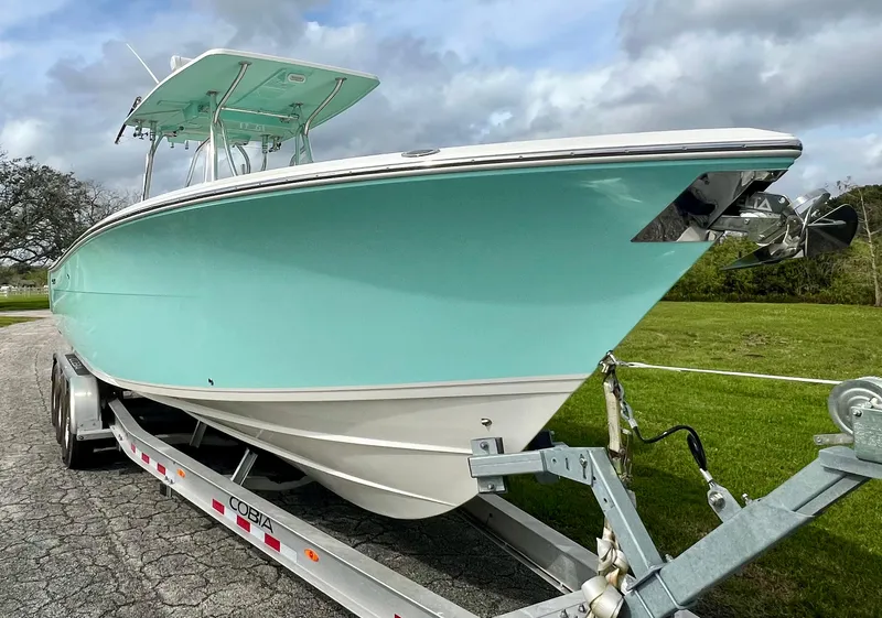 Slide: The Image of 2014 Cobia 296 Center Console boat on trailer, light blue hull, outdoor setting. - 5