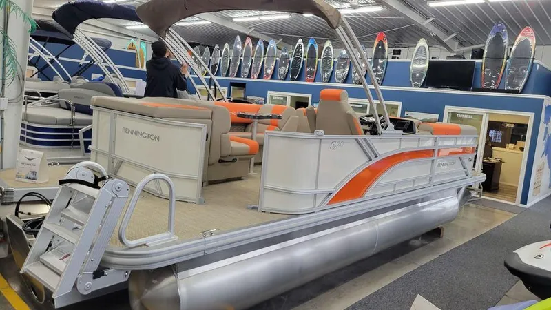 Slide: The Image of 2024 Bennington 20 SL pontoon boat with orange accents on display in a showroom. - 8