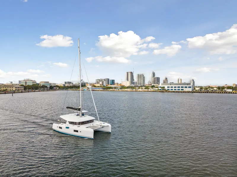Slide: The Image of 2018 Lagoon 42 catamaran sailing near a city skyline under a clear blue sky. - 14