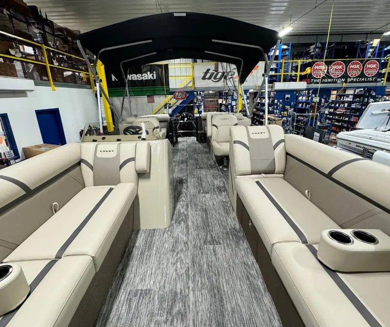 Slide: The Image of 2024 Crest Classic LX 240 pontoon boat interior with beige seating in showroom. - 2