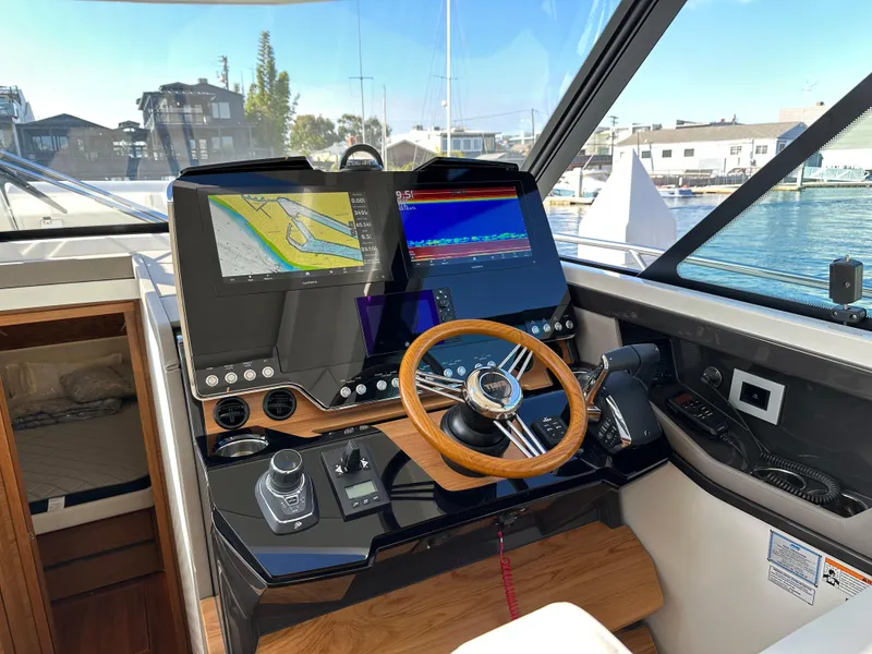 Slide: The Image of 2024 Tiara Yachts 48 LE helm with navigation screens and wooden steering wheel. - 44