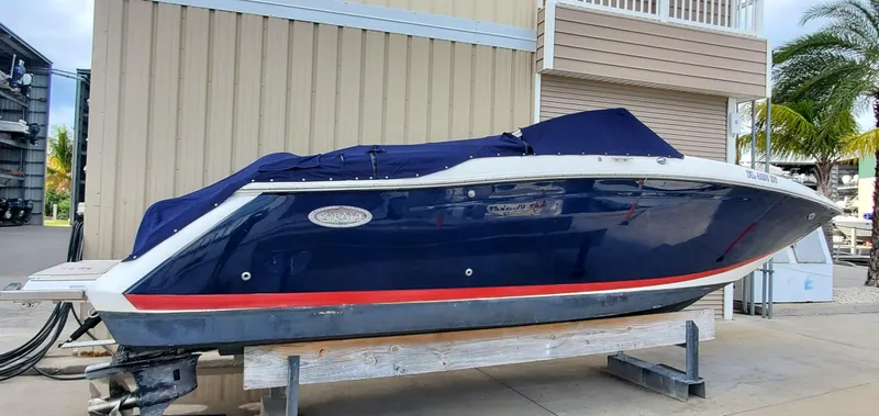 Slide: The Image of 2013 Cobalt 24SD boat with blue cover, docked outdoors near a building and palm tree. - 11