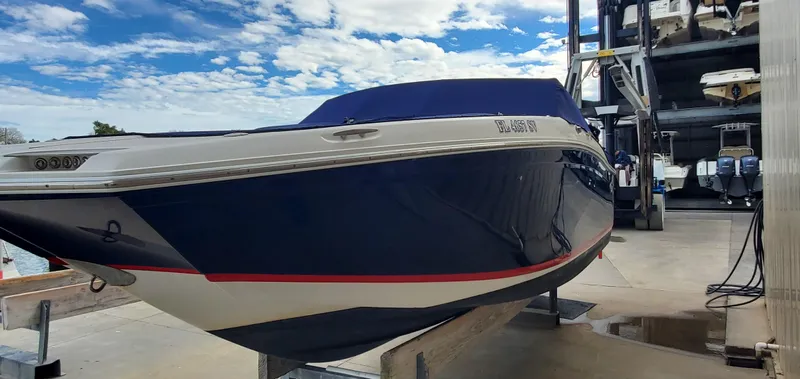 Slide: The Image of 2013 Cobalt 24SD boat in storage, blue hull, white trim, under a partly cloudy sky. - 15