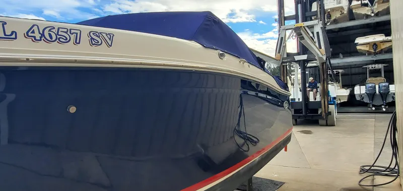 Slide: The Image of 2013 Cobalt 24SD boat in storage facility, blue hull, covered, with visible registration number. - 16