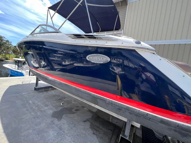 Slide: The Image of 2013 Cobalt 24SD boat with blue hull and red stripe, docked under a clear sky. - 3