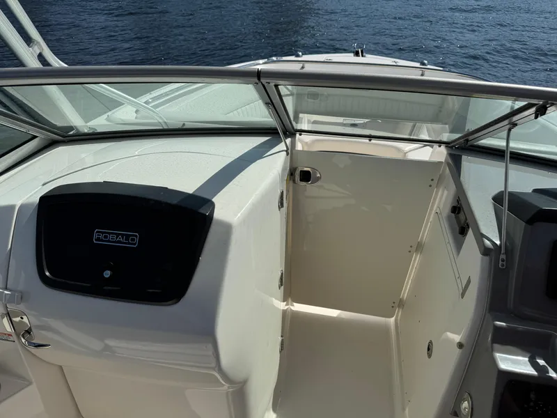 Slide: The Image of 2015 Robalo R247 Dual Console boat interior with open cabin door, on calm water. - 18