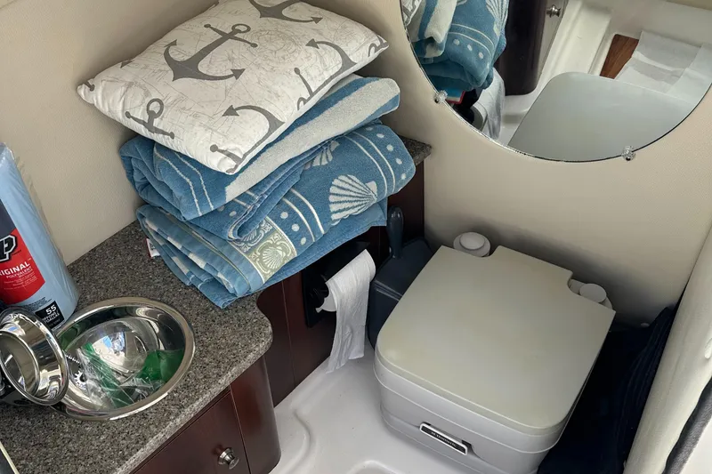 Slide: The Image of 2015 Robalo R247 Dual Console boat interior with sink, portable toilet, and nautical-themed linens. - 35