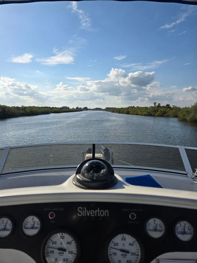 Slide: The Image of View from 1997 Silverton 372 Motor Yacht dashboard, cruising on a serene river under blue skies. - 24