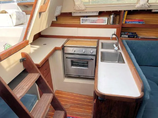 Slide: The Image of 1988 Catalina 30 MkII yacht interior with compact kitchen, stove, sink, and wooden accents. - 10