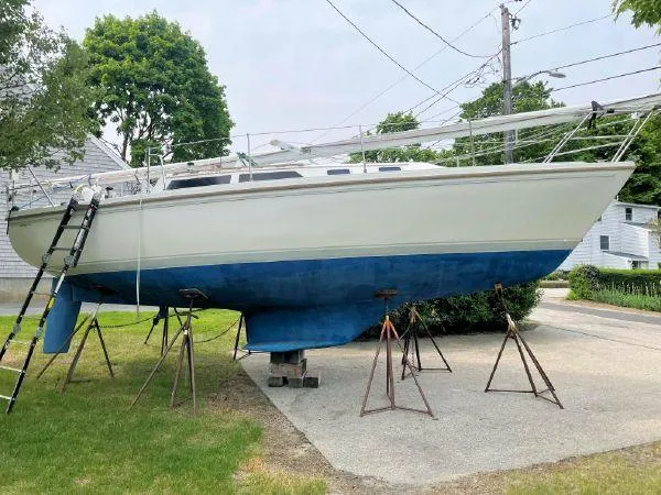 Slide: The Image of 1988 Catalina 30 MkII sailboat on stands, white hull, blue bottom, residential background. - 23