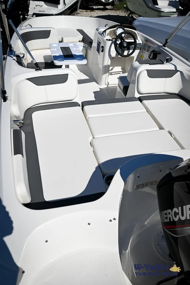 Slide: The Image of 2023 Bayliner E18 boat interior with white and gray seating, steering wheel, and Mercury engine. - 14