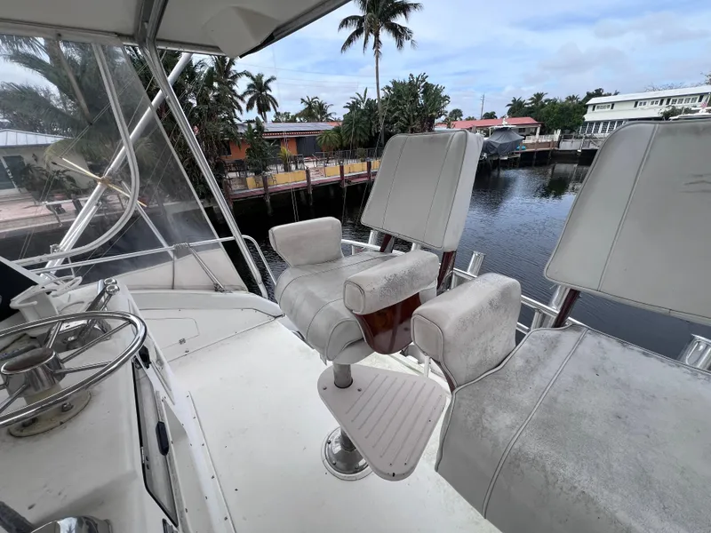 Slide: The Image of 1988 Bertram 43 Convertible boat helm with captain chairs, docked by waterfront homes. - 23