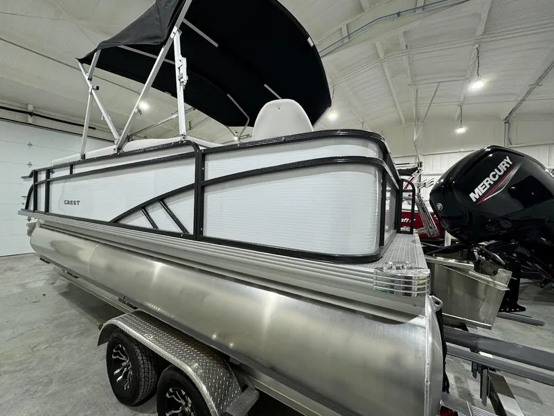 Slide: The Image of 2024 Crest Classic LX 220 pontoon boat with black canopy in indoor showroom. - 1