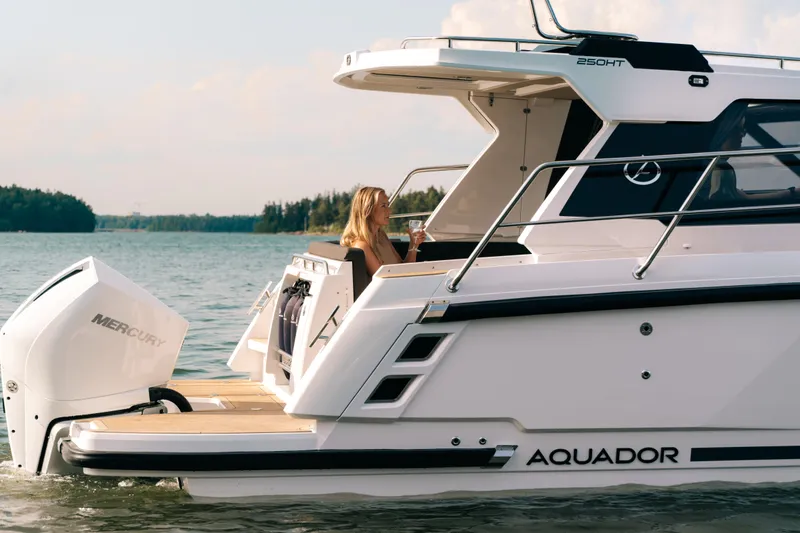 Slide: The Image of 2024 Aquador 250 HT boat cruising on a serene lake with a person relaxing onboard. - 6