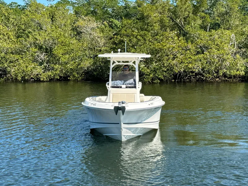 Slide: The Image of 2022 Boston Whaler 230 Outrage boat on calm water near lush greenery. - 4