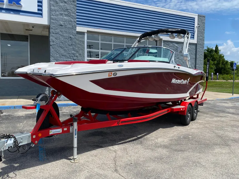 Slide: The Image of 2017 MasterCraft X26 boat on red trailer, parked outside a building. - 1