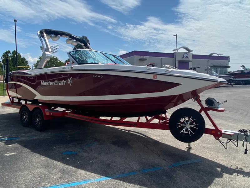 Slide: The Image of 2017 MasterCraft X26 boat on trailer, parked outdoors under a partly cloudy sky. - 2