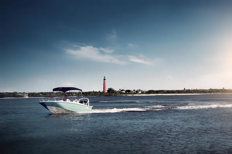 Slide: The Image of 2024 Boston Whaler 160 Super Sport cruising near a lighthouse on a sunny day. - 18