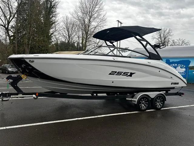 Slide: The Image of 2024 Yamaha Boats 255XD on trailer, sleek white design, black accents, parked outdoors. - 1