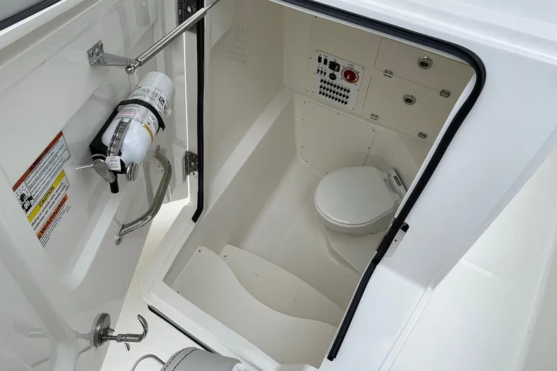 Slide: The Image of 2024 Pursuit S 248 Sport boat interior with a compact marine toilet and fire extinguisher. - 13
