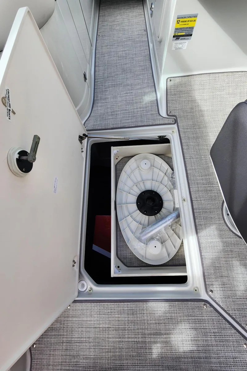 Slide: The Image of 2024 Crownline E235 boat storage compartment with open hatch and coiled hose. - 13