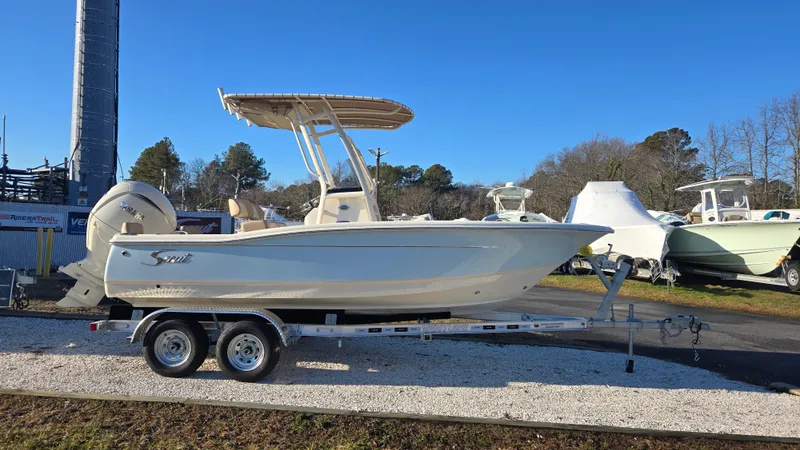 Slide: The Image of 2025 Scout 195 Sportfish boat on trailer, parked outdoors under clear blue sky. - 2
