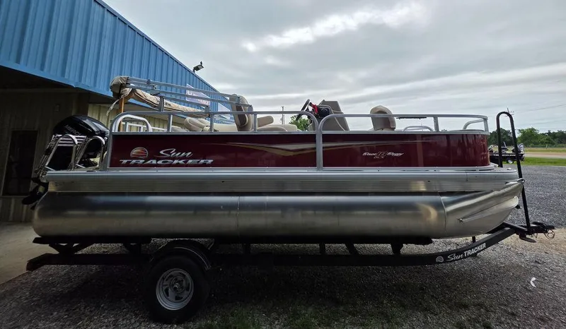 Slide: The Image of 2025 Sun Tracker BASS BUGGY® 18 DLX pontoon boat on trailer, parked outdoors. - 23