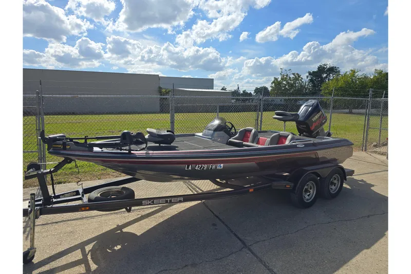 The Image of 2003 Skeeter SX200 boat on trailer, parked outdoors under a partly cloudy sky. - 0